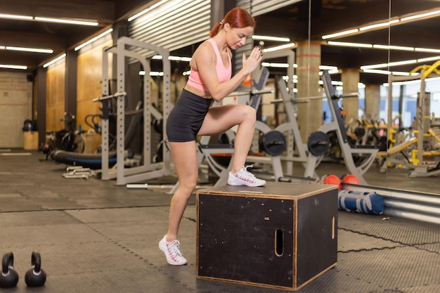 Donna in forma in abbigliamento sportivo passi su scatola di legno in palestra allenamento funzionale intensivo