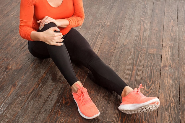 Photo fit woman in tight sportswear holding painful knee sitting on floor at home gym, suffering muscle strain, sprain ligaments or joint injury, health problems after sports training. indoor studio shot