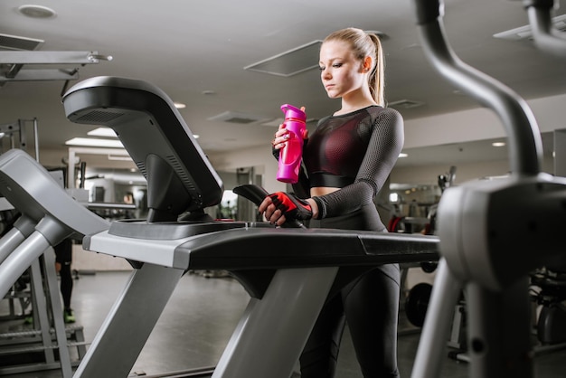 Fit woman on treadmill with bottlw of water in the gym