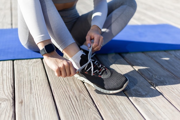 Fit woman tying shoelaces while sitting on a mat on the beach on a bright sunny day Healthy lifestyle