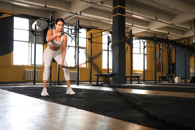 Fit woman using battle ropes during strength training at the gym.