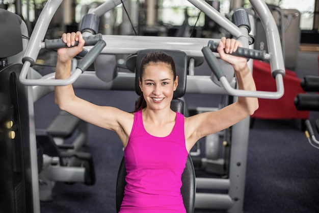 Fit woman using weight machine in gym