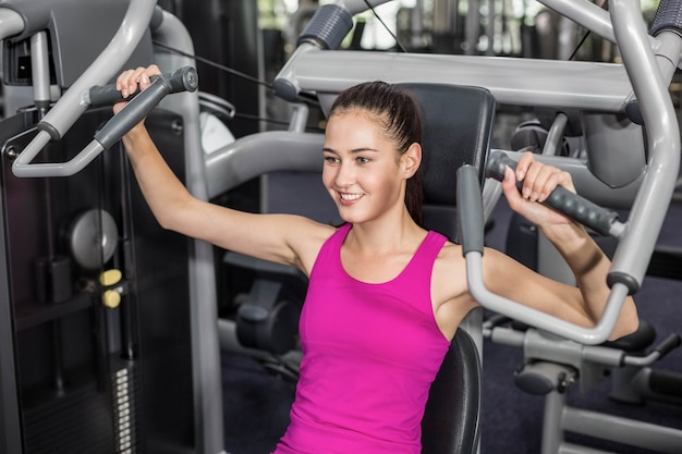 Fit woman using weight machine in gym