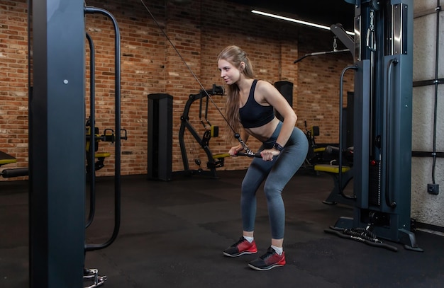 체육관에서 케이블 운동 기계와 함께 완벽한 신체 훈련 삼두근을 가진 맞는 여자