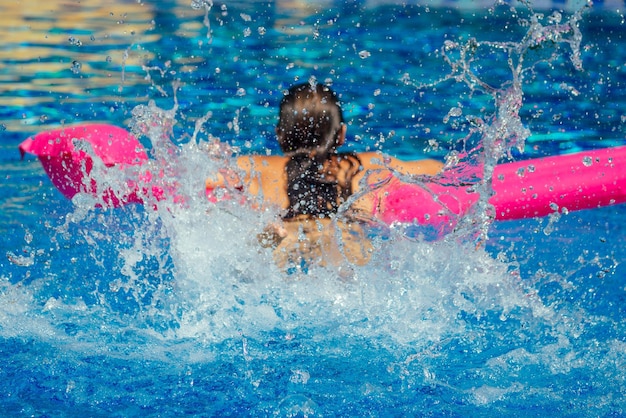 Donna in forma che lavora in piscina. giovane bella ragazza che fa esercizio di acquagym galleggiante su uno spruzzo d'acqua gonfiabile rosa materasso