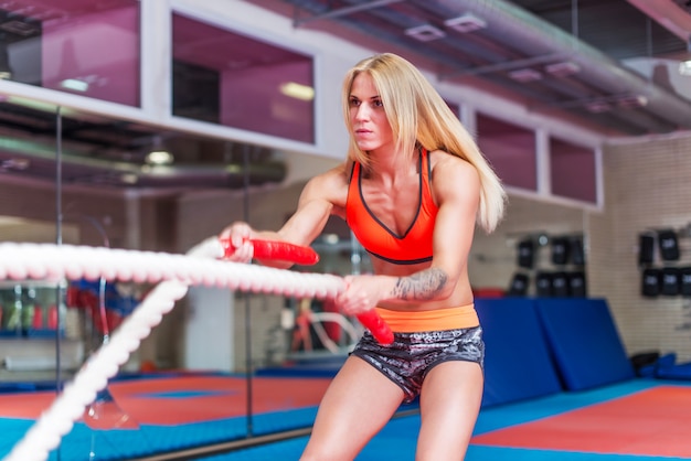 Fit woman working out with battle ropes at a gym.