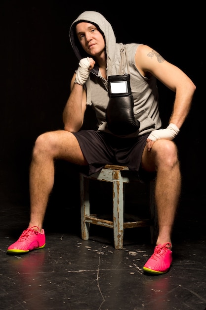 Fit young boxer sitting waiting for a fight on a wooden stool