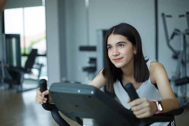 Fit young girl using exercise bike at the gym. Fitness female using air bike at gym.