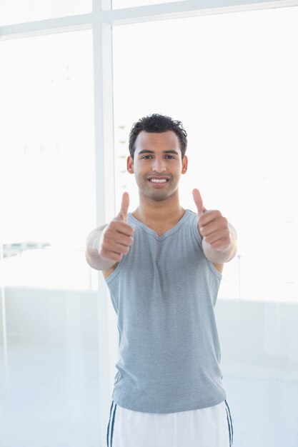 Fit young man gesturing thumbs up in fitness studio