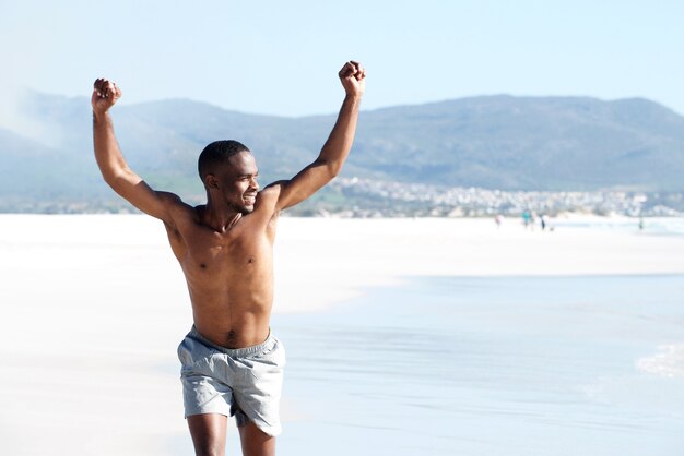 Fit young man running on the beach with arms raised in victory