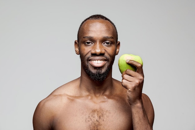 Fit young man with beautiful torso with green apple isolated on gray background