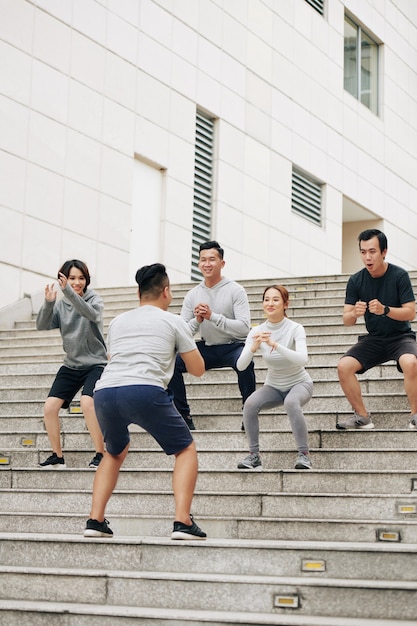 Fit young vietnamese people repeating after coach when doing squats on steps outdoors