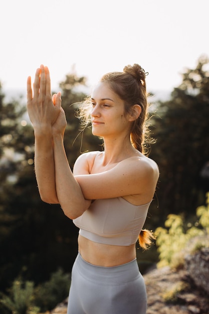 Fit young woman practices yoga on the rocks against the background of the pine forest