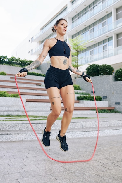 Fit young woman in short and sports bra jumping with skipping rope