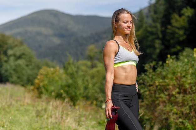 Fit young woman stretching legs and looking at camera. Caucasian female exercising at the park in morning. drinking water