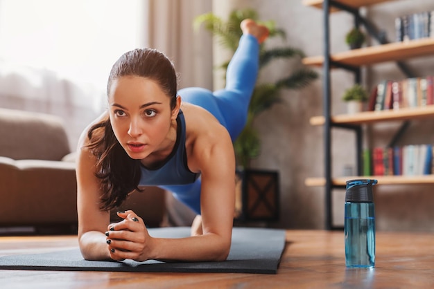 Fit young woman wearing sportswear working out at home on mat