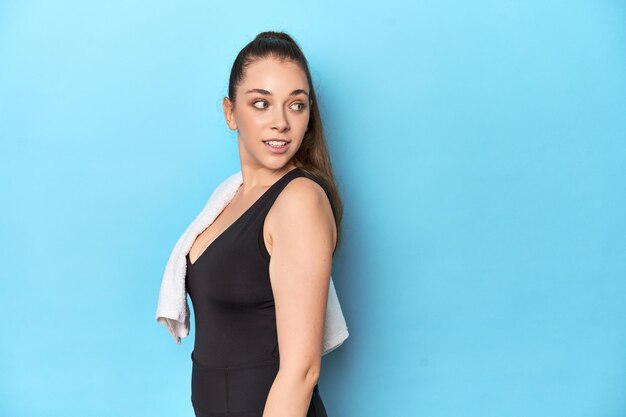 Fit young woman with a towel on her shoulder studio shot looks aside smiling cheerful and pleasant