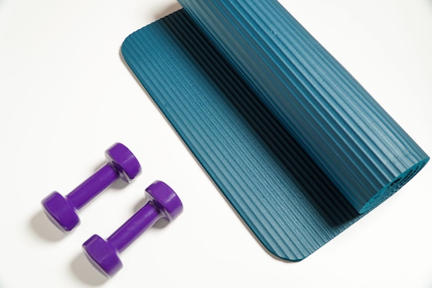 Fitness accessories conceptpurple dumbbell sport with blue yoga mat on white background copy space flat lay view from above