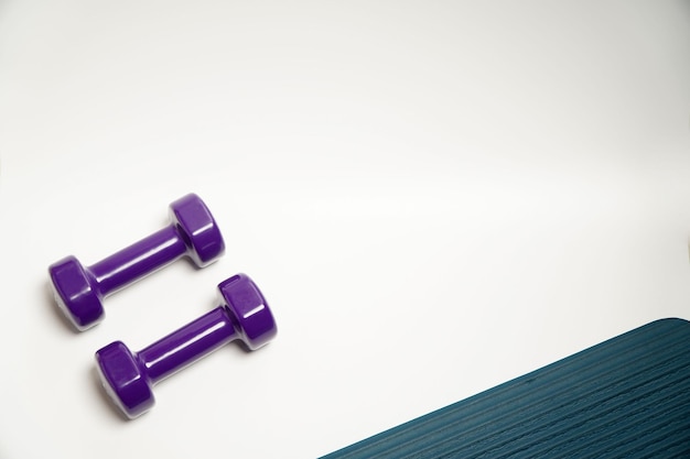 Fitness accessories conceptpurple dumbbell sport with blue yoga mat on white background copy space flat lay view from above