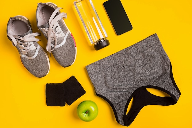 Accessori per il fitness su uno sfondo giallo sneakers bottiglia d'acqua smart e sport top