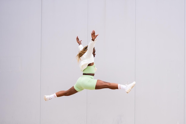 Fitness african woman jumping in front of an urban wall