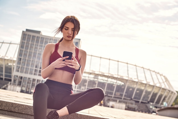 Fitness app close up photo of attractive and slim woman in sexy sportswear sitting on