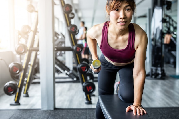 Гантель азиатской девушки фитнеса поднимаясь на спортзале.