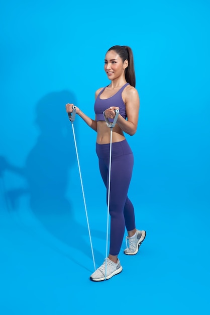 Fitness asian woman in sportswear exercising with a resistance band on blue background