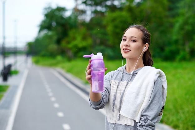 Fitness Aziatische vrouw met fles en handdoek water na hardlooptraining in zomerpark