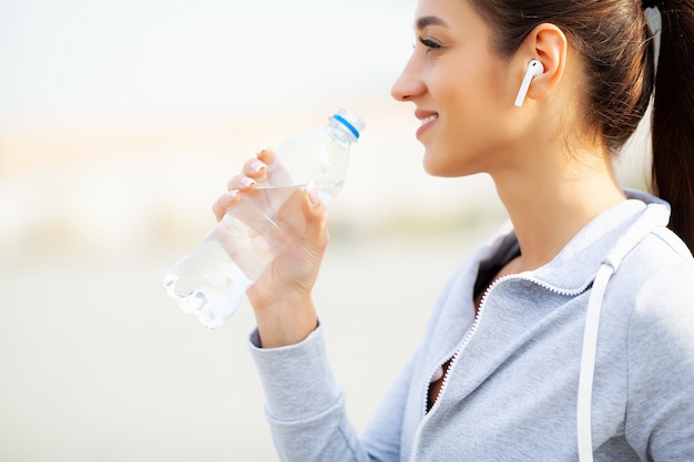 Fitness. Beautiful woman drinking water and listen to music after running