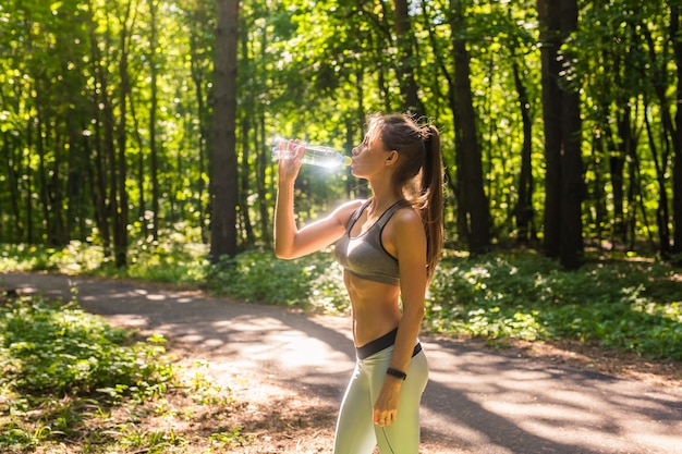 公園で夏の暑い日に運動した後、水を飲んで汗をかくフィットネス美女