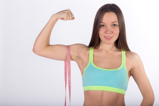 Foto la bella donna di forma fisica in abbigliamento sportivo misura il muscolo bicipite con la vista frontale del fondo bianco del nastro di centimetro