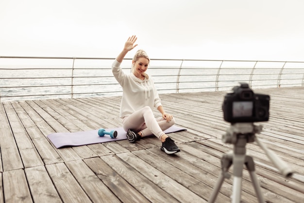 Fitness bloggen. Jonge gezonde sportvrouw die zichzelf opneemt op camera met statief op het strand. vloggen