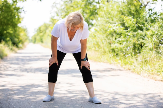 Foto fitness blonde vrouw moe na het joggen in het bos op de weg rust haar armen op haar knieën te houden met sportkleding en slim horloge op haar hand hoge kwaliteit foto