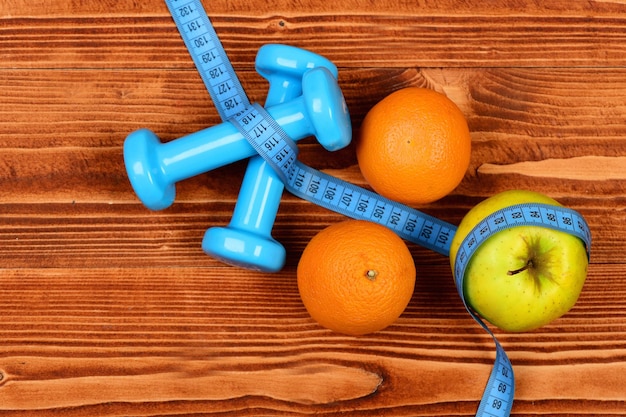 Fitness body concept, dumbbells weight with measuring tape, orange and apple fruit on brown vintage wooden background