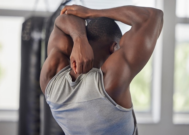 Fitness bodybuilder and black man stretching at gym for training exercise and workout for strong powerful muscles Back view sports and healthy athlete starting biceps triceps and elbow warm up