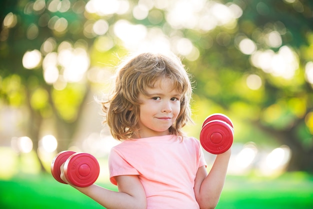 Фитнес-детский портрет спортивного маленького мальчика с гантелями в парке, тренировка в тренажерном зале, ребенок-спортсмен, ребенок