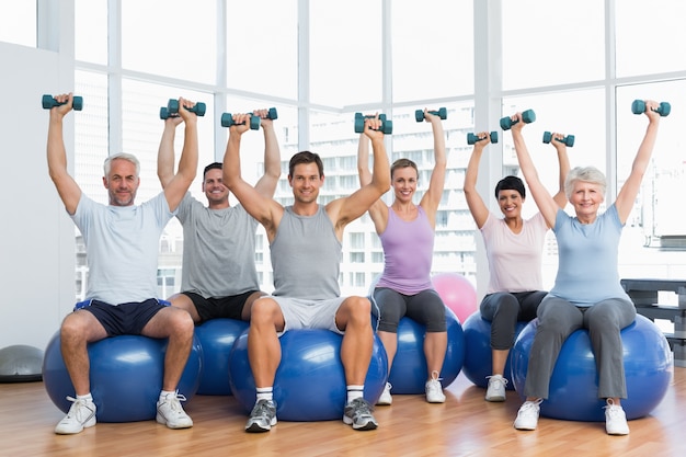 Fitness class with dumbbells sitting on exercise balls in gym