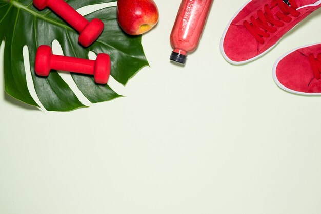 Fitness concept. sneakers, apple, dumbbell and fruit juice bottle on pastel color background