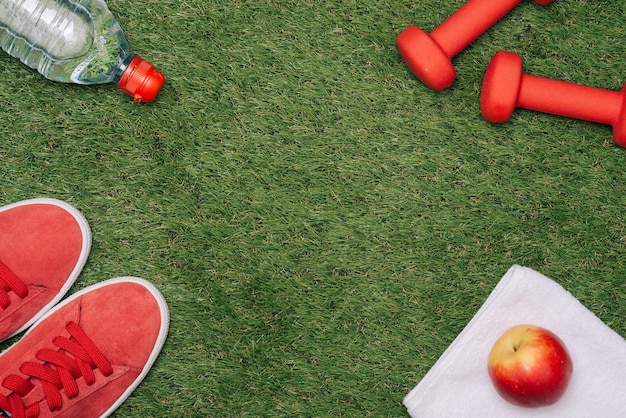 Fitness concept with Exercise Equipment, shoes, apple, Dumbbell and water on green grass.