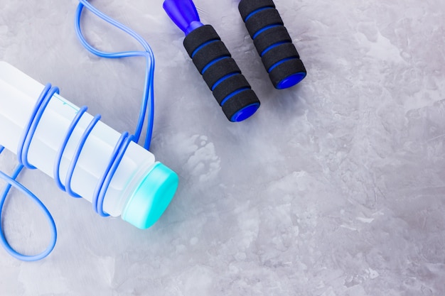 Fitness concept with jump rope and bottle of water. Sports equipment on a gray background. Healthy lifestyle concept. . Top view