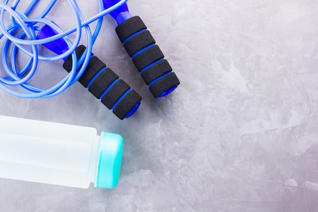 Fitness concept with jump rope and bottle of water. Sports equipment on a gray background. Healthy lifestyle concept. . Top view