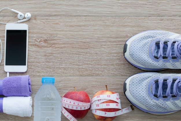 Photo fitness concept with running shoes, towel, bottle of water, apple, measuring tape, mobile phones view from above