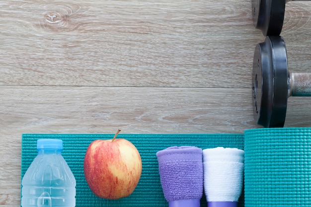 Concetto di fitness con asciugamano, bottiglia d'acqua, mela, manubrio, tappetino yoga. vista dall'alto