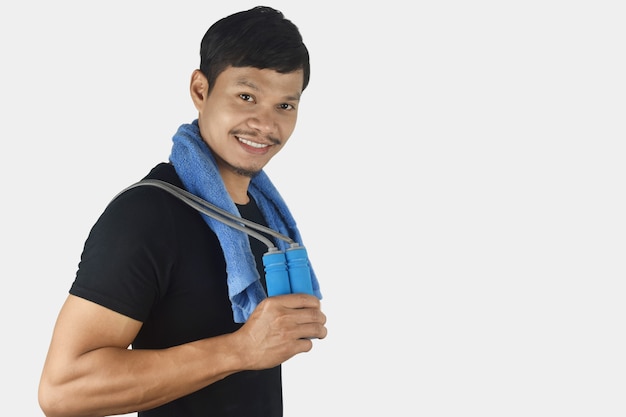 Fitness concept young man holding jumping rope at his shoulders on grey background