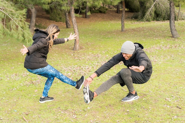 Foto coppia fitness in vestiti caldi in piedi su una gamba e allungando l'altra. coppia multietnica all'aperto.