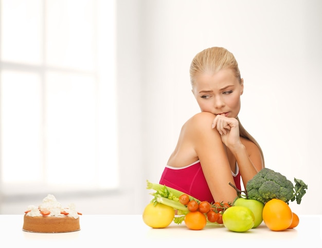 fitness, dieet, gezondheid en voedselconcept - twijfelende vrouw met fruit en taart
