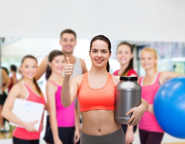 fitness and diet concept - smiling teenage girl with jar of protein showing thumbs up