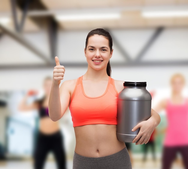 fitness and diet concept - smiling teenage girl with jar of protein showing thumbs up