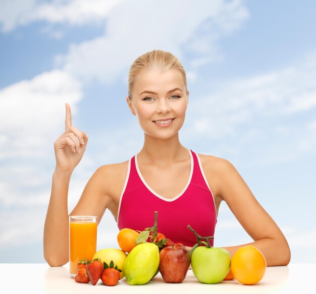 fitness, diet and food concept - young woman with organic food or fruits holding finger up